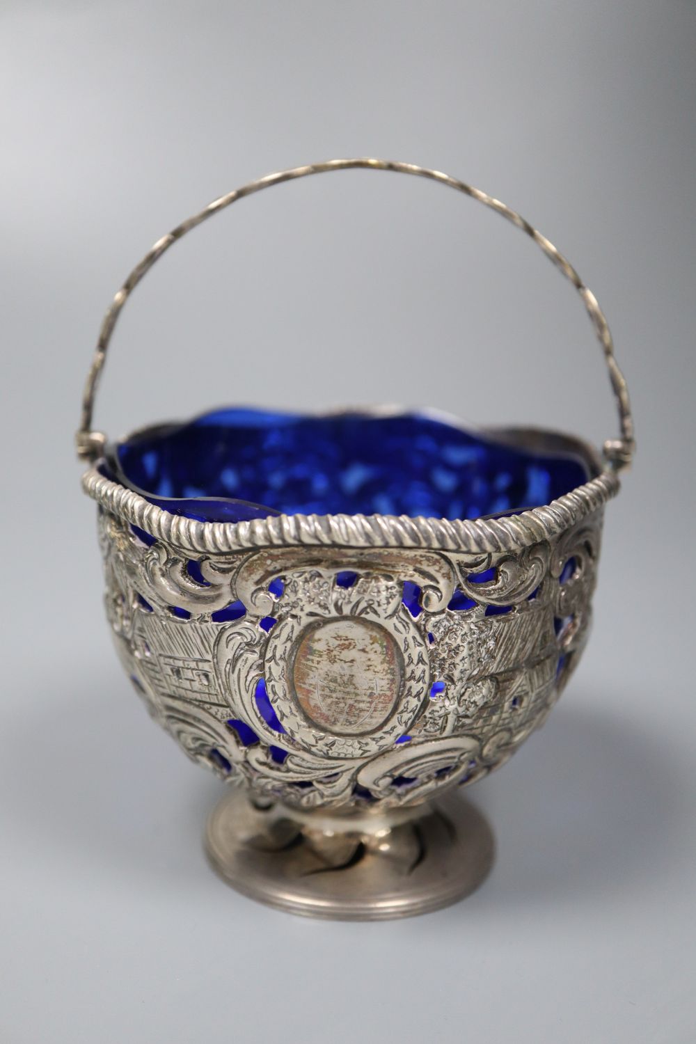 An Edwardian silver sugar basket, George V silver bon-bon dish, silver mounted match strike and a mug salt and spoon (4)